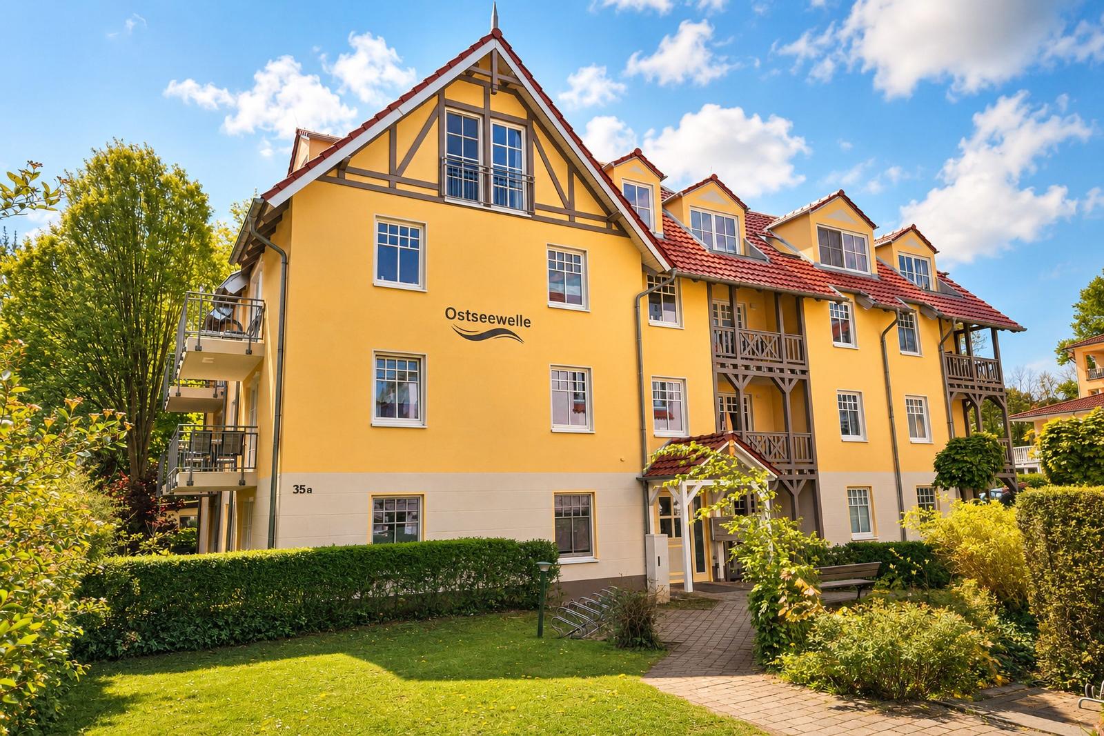 Gelbes Mehrfamilienhaus mit Balkonen und rotem Dach unter blauem Himmel.