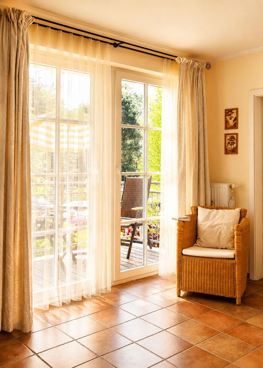 Ein Raum mit Terrassentür, Wickerstuhl und Terrasse mit Gartenmöbeln.