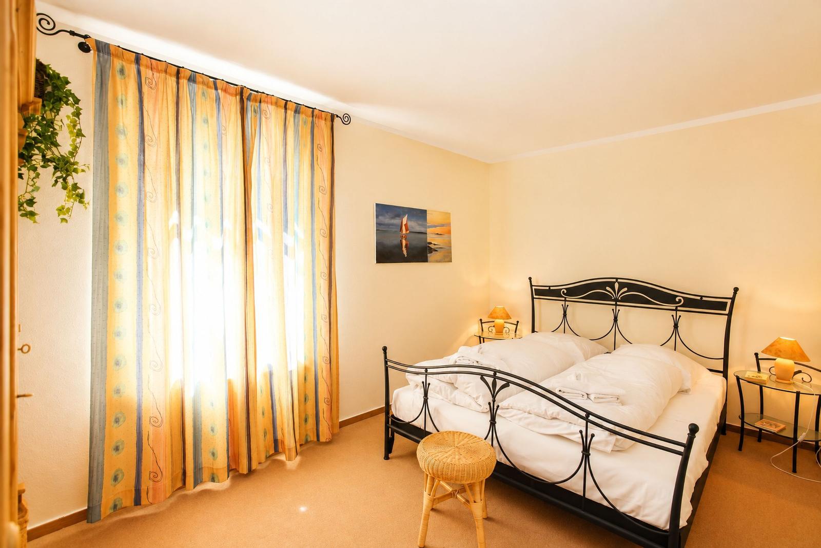 Schlafzimmer mit Doppelbett, Vorhängen und Nachttischen.