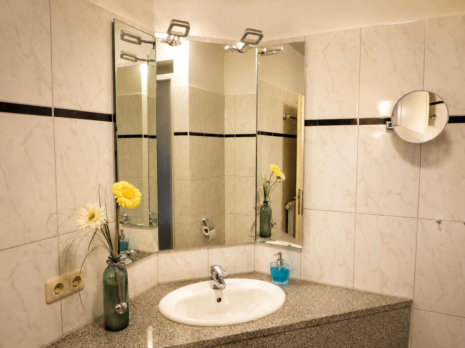 Badezimmer mit Waschbecken, Spiegeln und Blumen in Vase