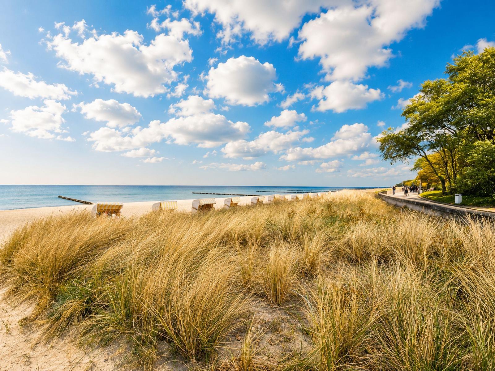 Strand mit Dünen, Strandkörben und blauem Himmel mit weißen Wolken.