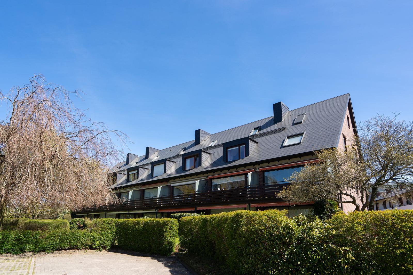 Ein mehrstöckiges Haus mit Balkonen und dunklem Dach unter blauem Himmel.