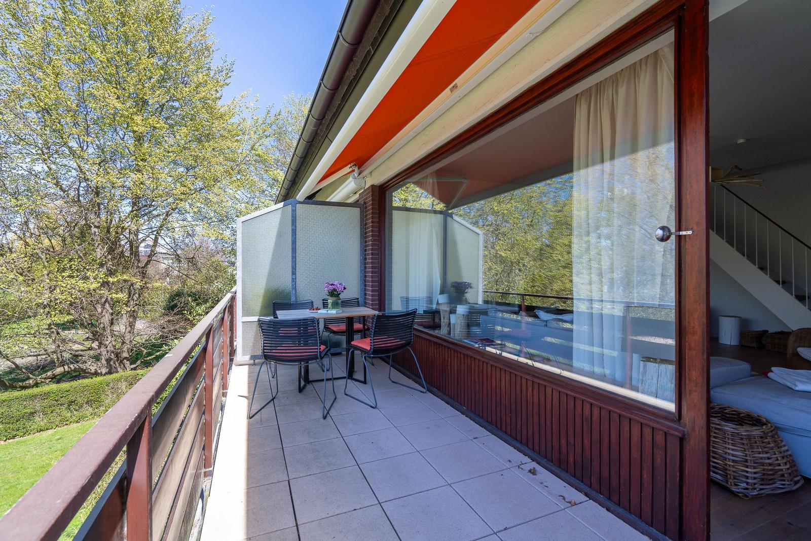 Terrasse mit Tisch, Stühlen und Blick auf Grünflächen. Glaswand führt ins Haus.