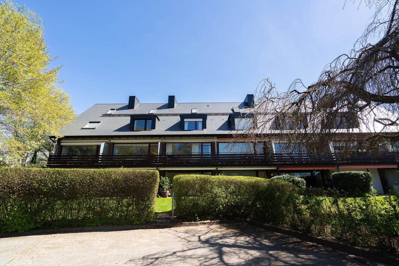 Ein zweistöckiges Haus mit Balkon und Dachfenstern. Umgeben von Bäumen und Hecken.