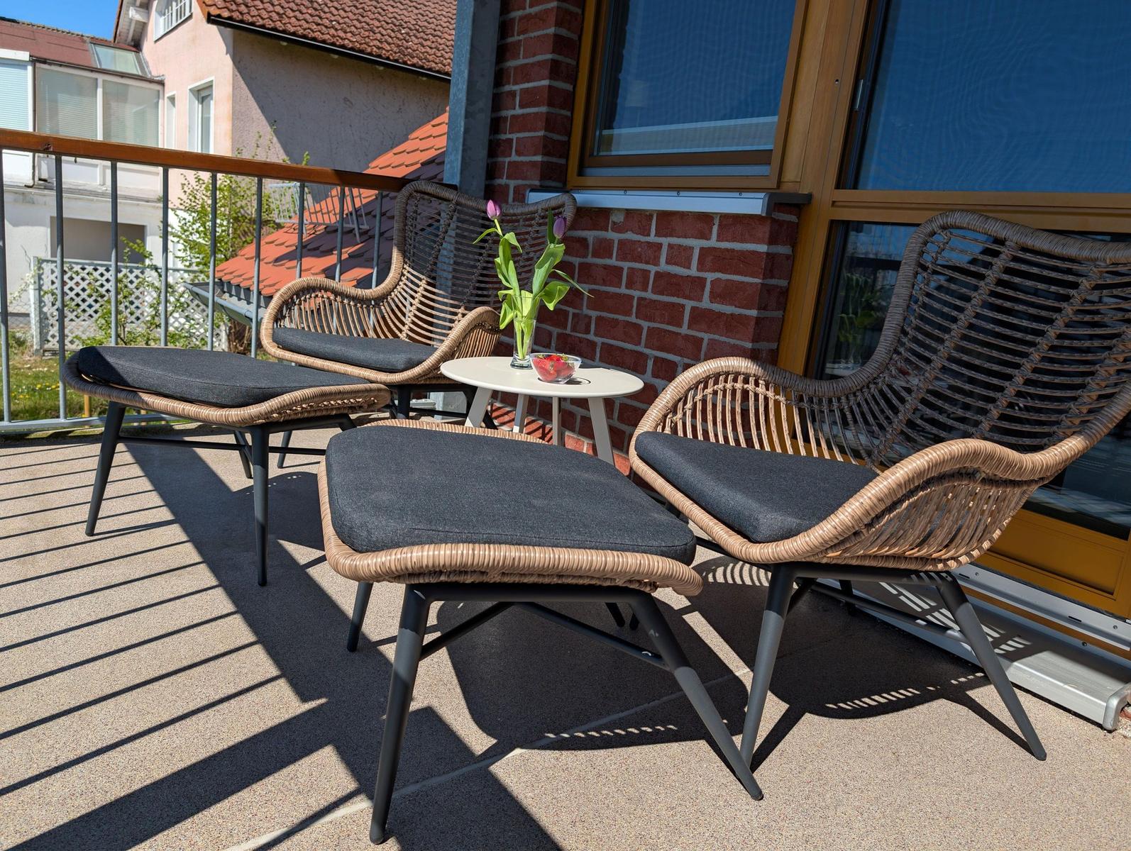 Terrasse mit zwei Rattan-Stühlen, Fußhocker und kleinem Tisch mit Blumen.