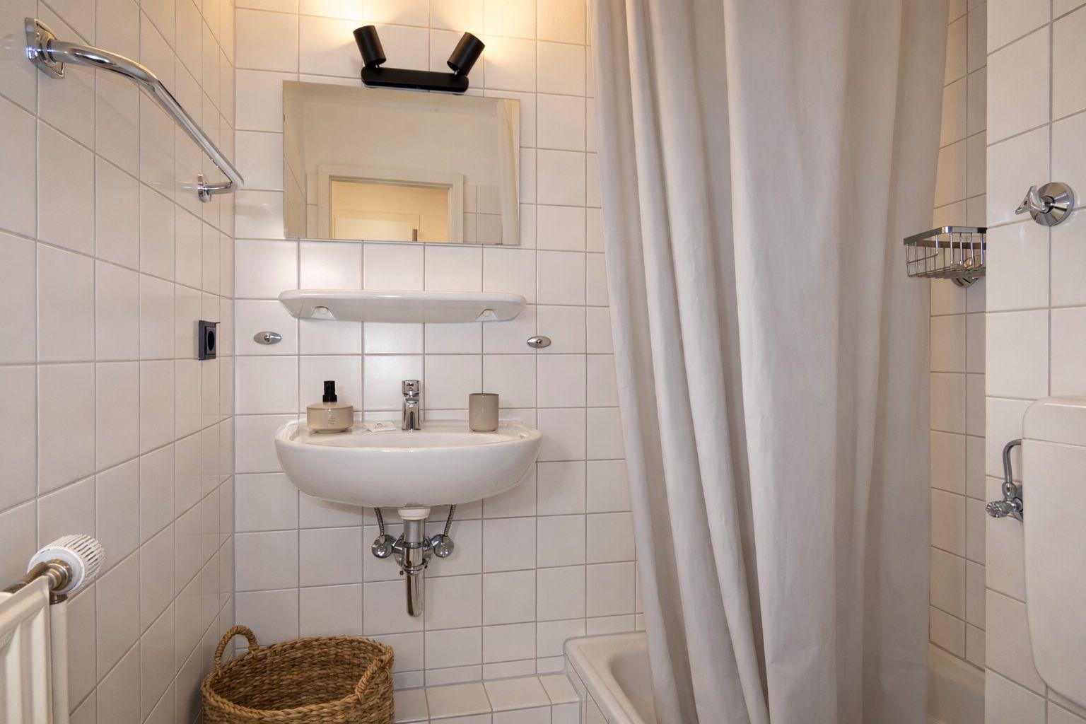 Badezimmer mit Waschbecken, Spiegel, Duschvorhang und Badewanne.