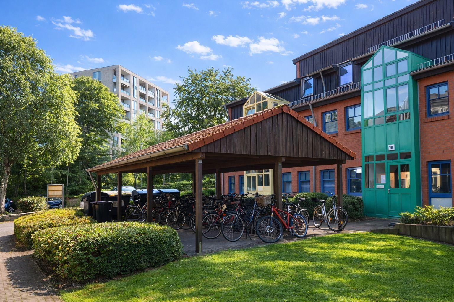 Haus mit Fahrradabstellplatz unter Dach und grüner Rasenfläche.