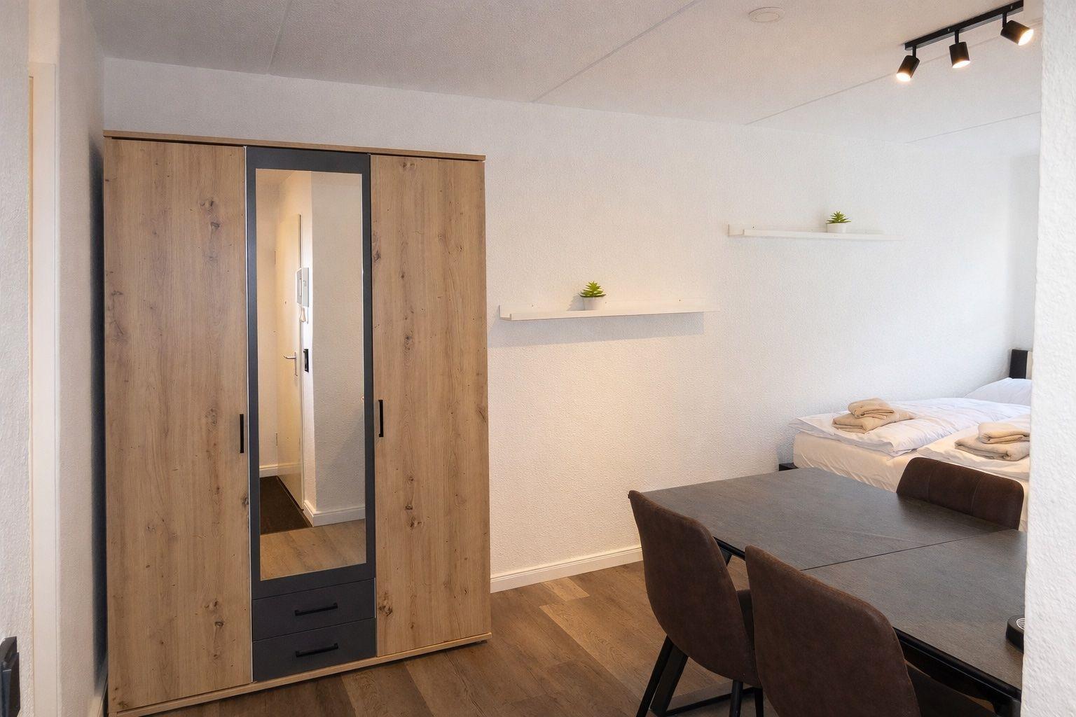 Schlafzimmer mit Tisch, Stühlen und Kleiderschrank. Wandregale mit Pflanzen.