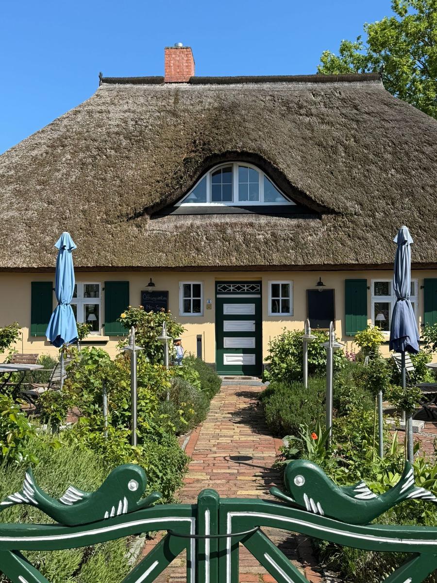Haus mit Strohdach, grüner Tür und gepflasterter Weg durch den Garten.