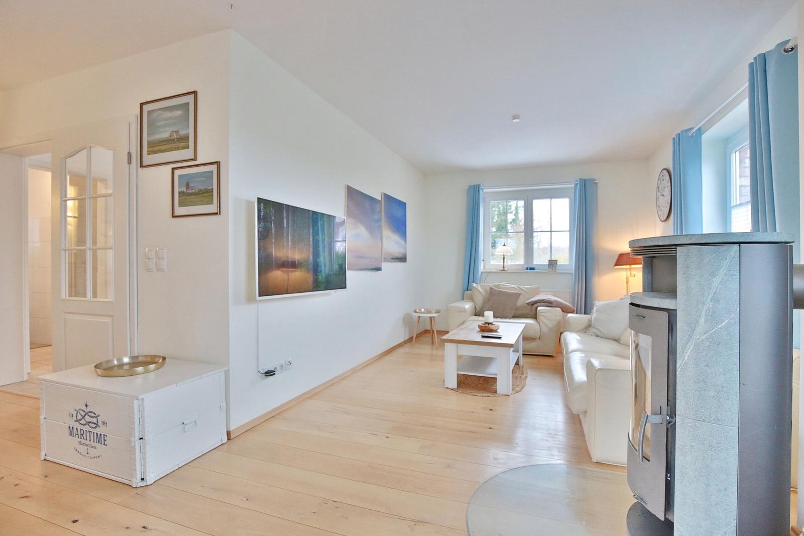 Wohnzimmer mit Sofa, Couchtisch und Kaminofen. Holzboden und Wandbilder sichtbar.