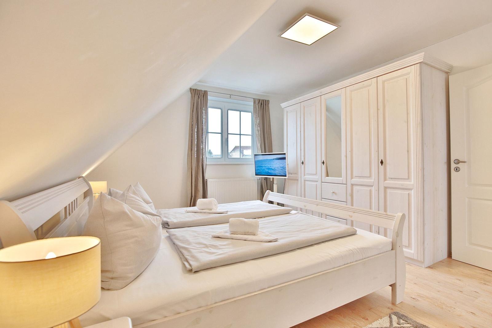 Schlafzimmer mit Doppelbett, Kleiderschrank und Fenster.