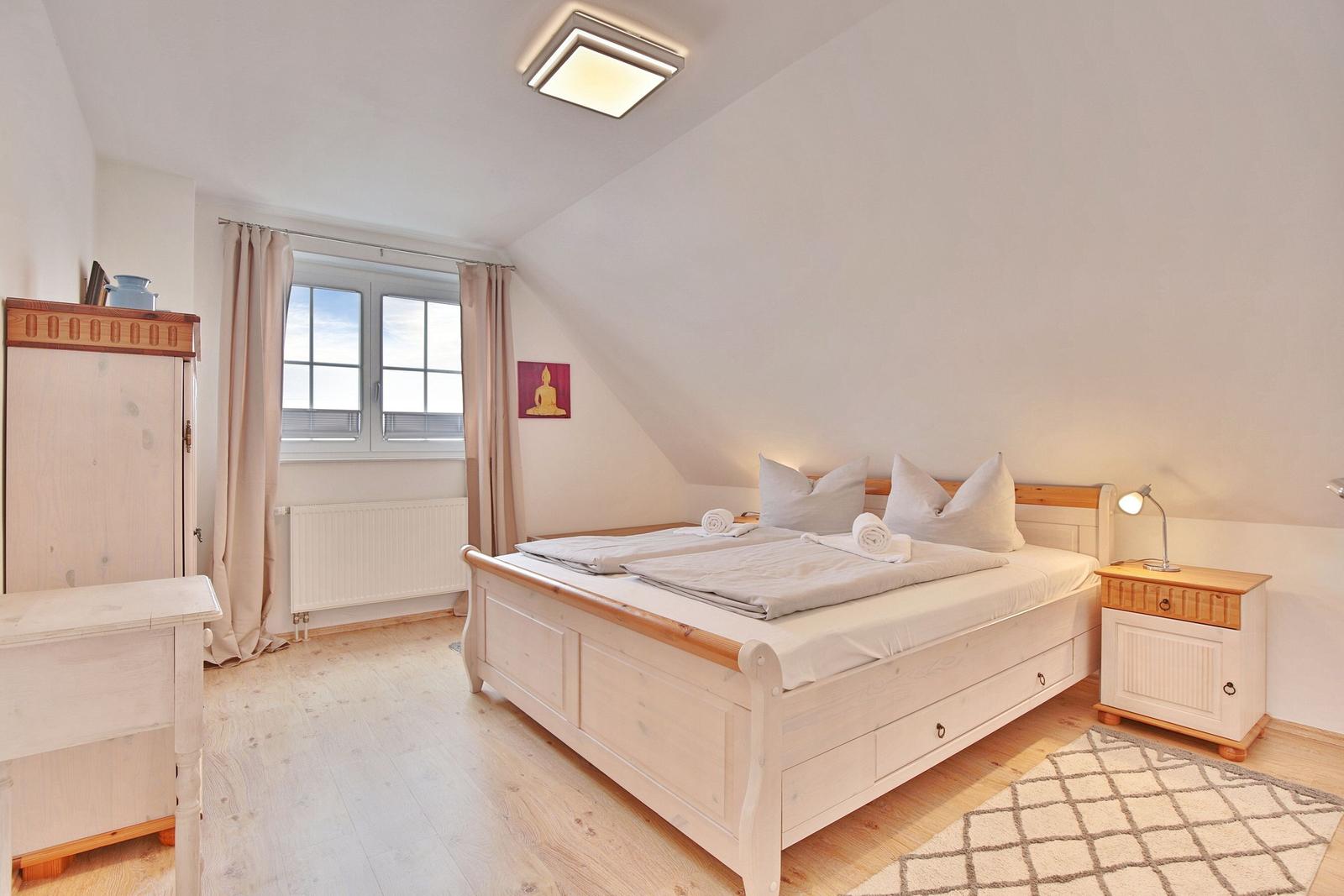 Schlafzimmer mit Dachschrägen, Bett, Nachttisch und Fenster.