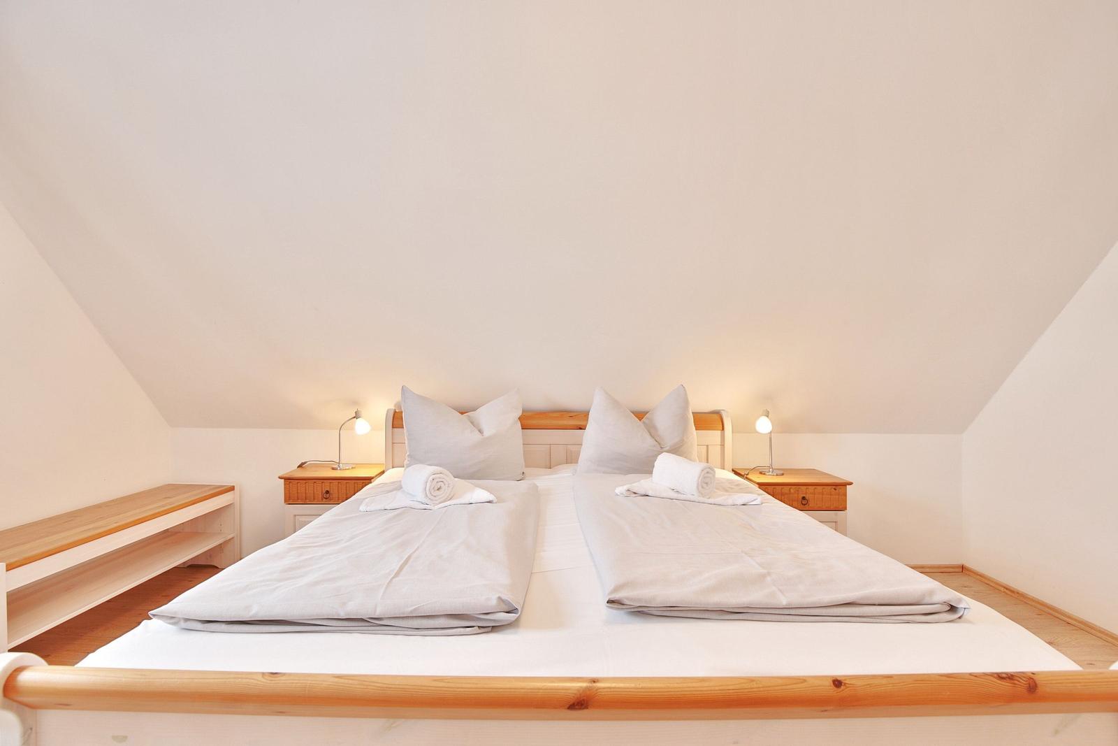 Zimmer mit Doppelbett, zwei Nachttischen und Rolladen. Dachgeschoss mit schrägen Wänden.