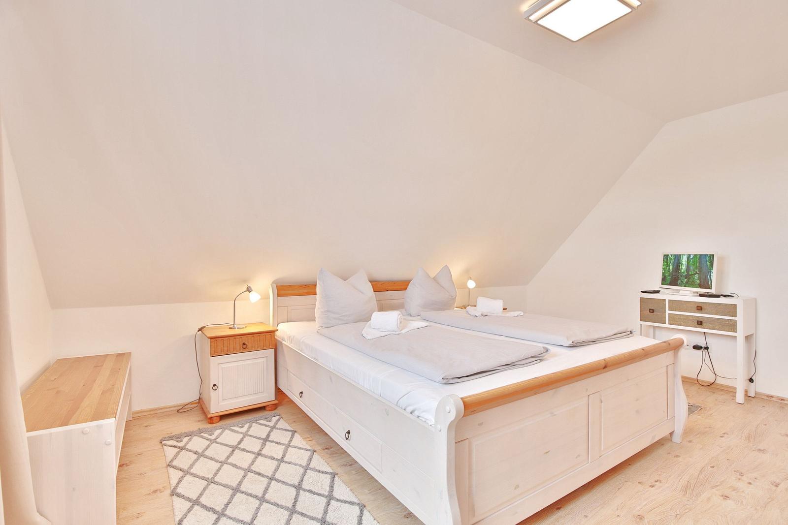Schlafzimmer mit Doppelbett, Nachttisch, Schreibtisch und Fernseher.