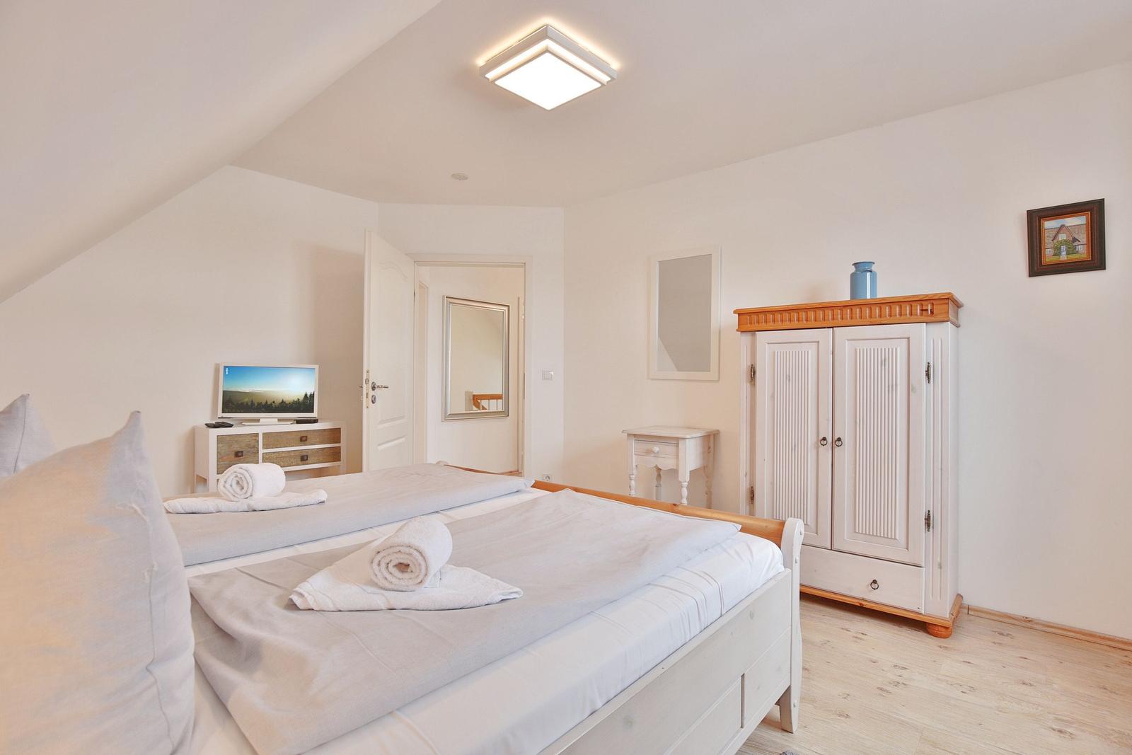 Schlafzimmer mit Doppelbett, Kleiderschrank und Fernseher.