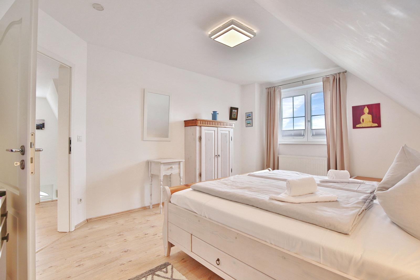 Schlafzimmer mit Doppelbett, Kleiderschrank und Fenster mit Blick nach draußen.