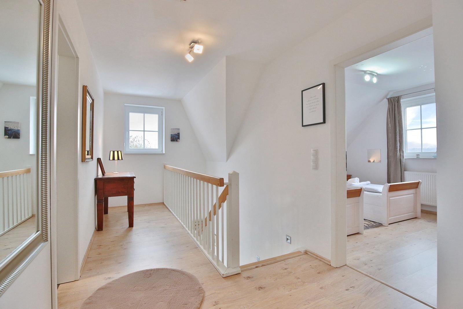 Flur mit Holzboden, Treppe und Blick in Schlafzimmer mit Bett und Fenster.