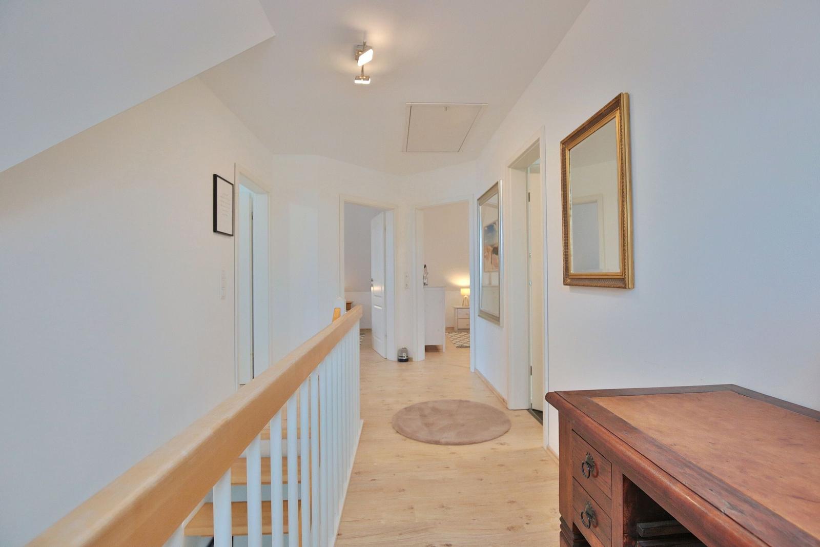 Flur mit Holzboden, Spiegel und Schrank. Treppe mit weißer Brüstung führt nach oben.
