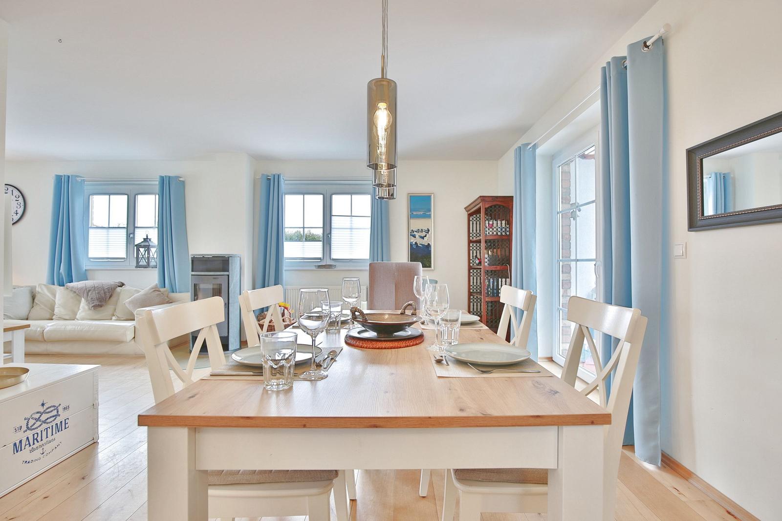 Esszimmer mit Holztisch, Stühlen und Fenstern mit blauen Vorhängen.