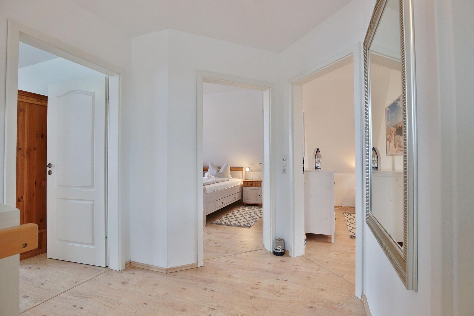 Flur mit Blick in Schlafzimmer und Badezimmer, Holzboden und weiße Wände.