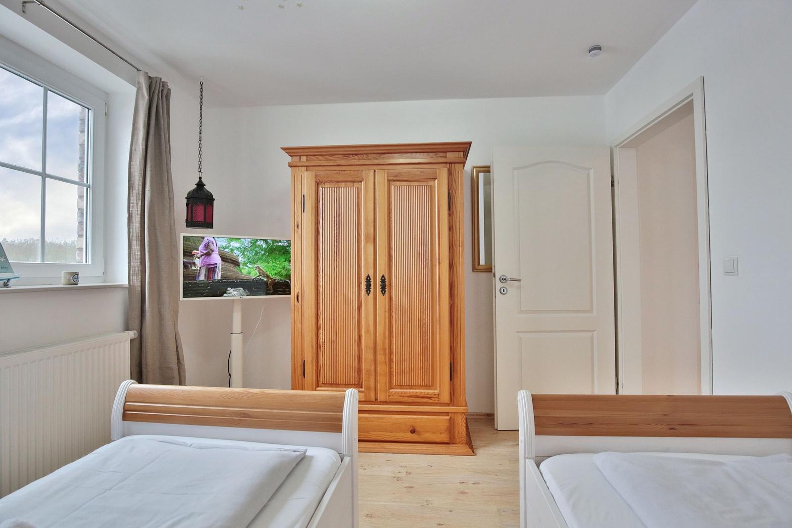 Zwei Betten, Holzschrank, Fenster mit Vorhang und TV.