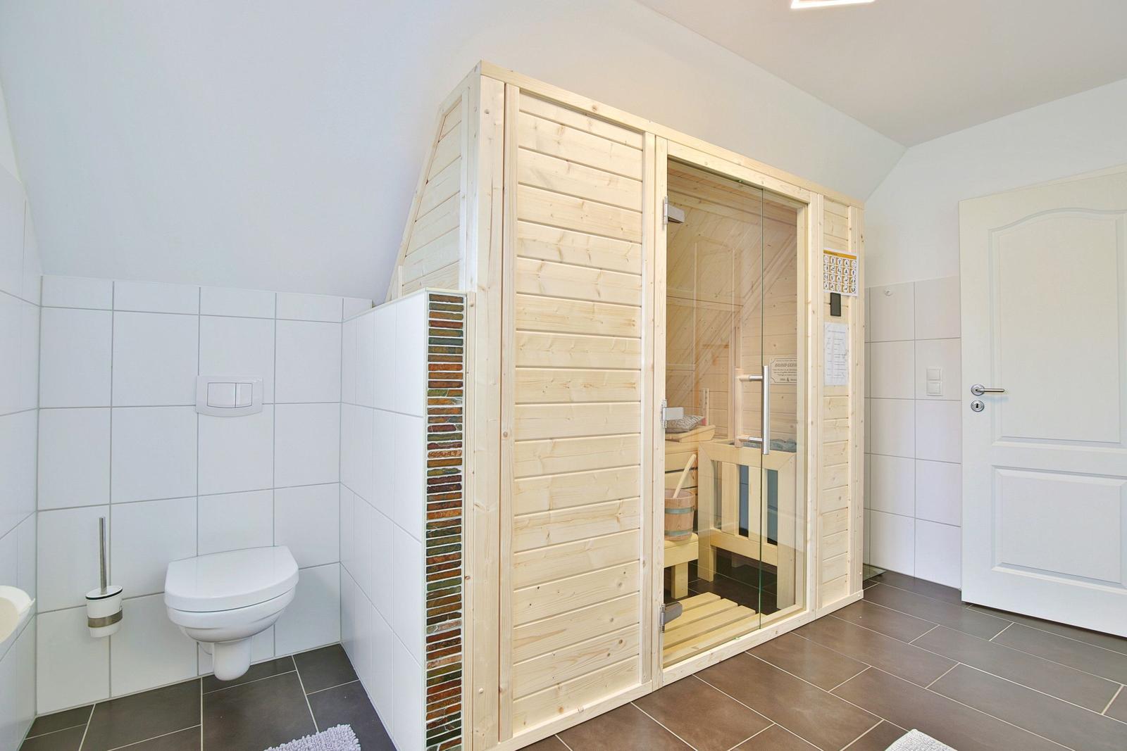 Dusche, Toilette und Sauna in einem Raum mit weißen Wänden und braunem Bodenfliesen.