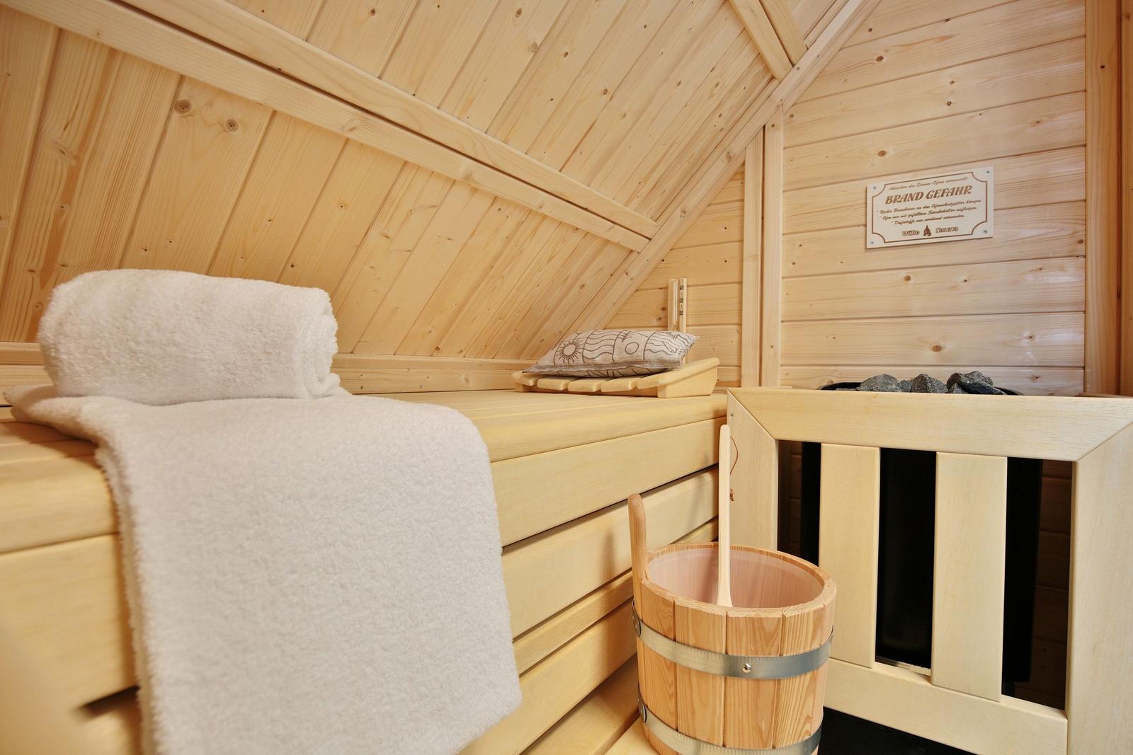 Holzsauna mit Liege, Handtuch und Eimer. Wandtafel mit Warnhinweis.