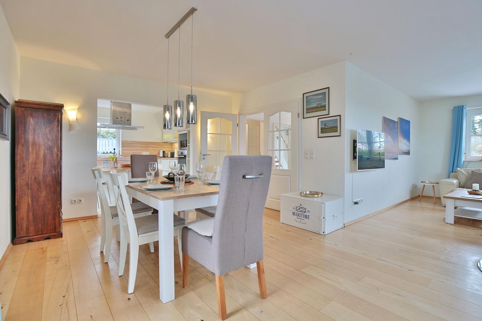 Essbereich mit Tisch und Stühlen, Küche im Hintergrund, Wohnzimmer mit Sofa und Fernseher.