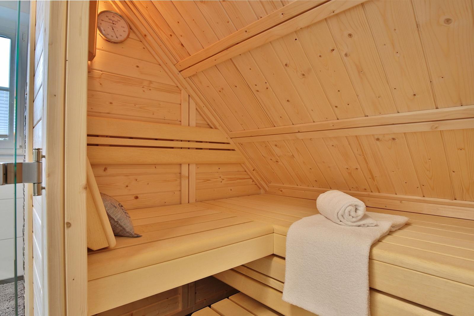 Holzsauna mit Sitzbänken, Handtuch und Thermometer an der Wand.