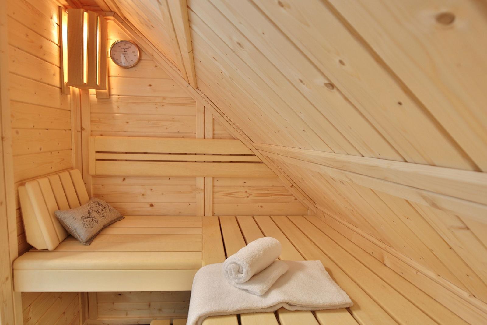 Sauna mit Holzbank, Kissen und Handtuch. Thermometer und Licht an der Wand.