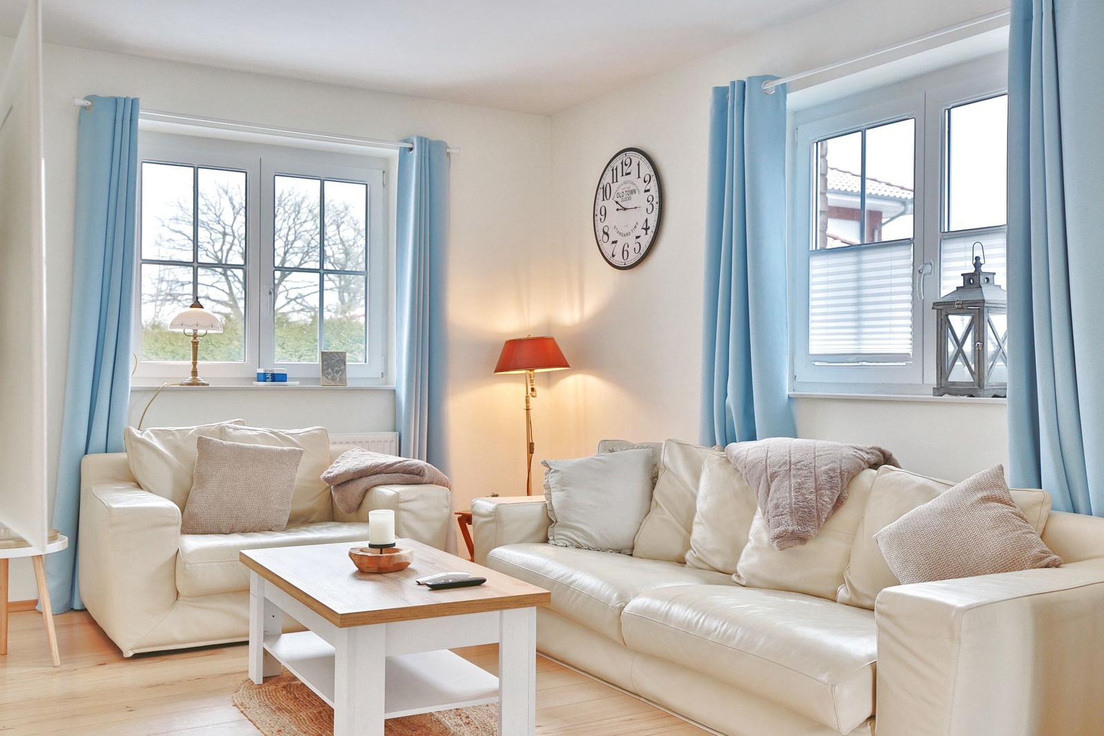 Wohnzimmer mit cremefarbenen Sofas, Holztisch und blauen Vorhängen an den Fenstern.