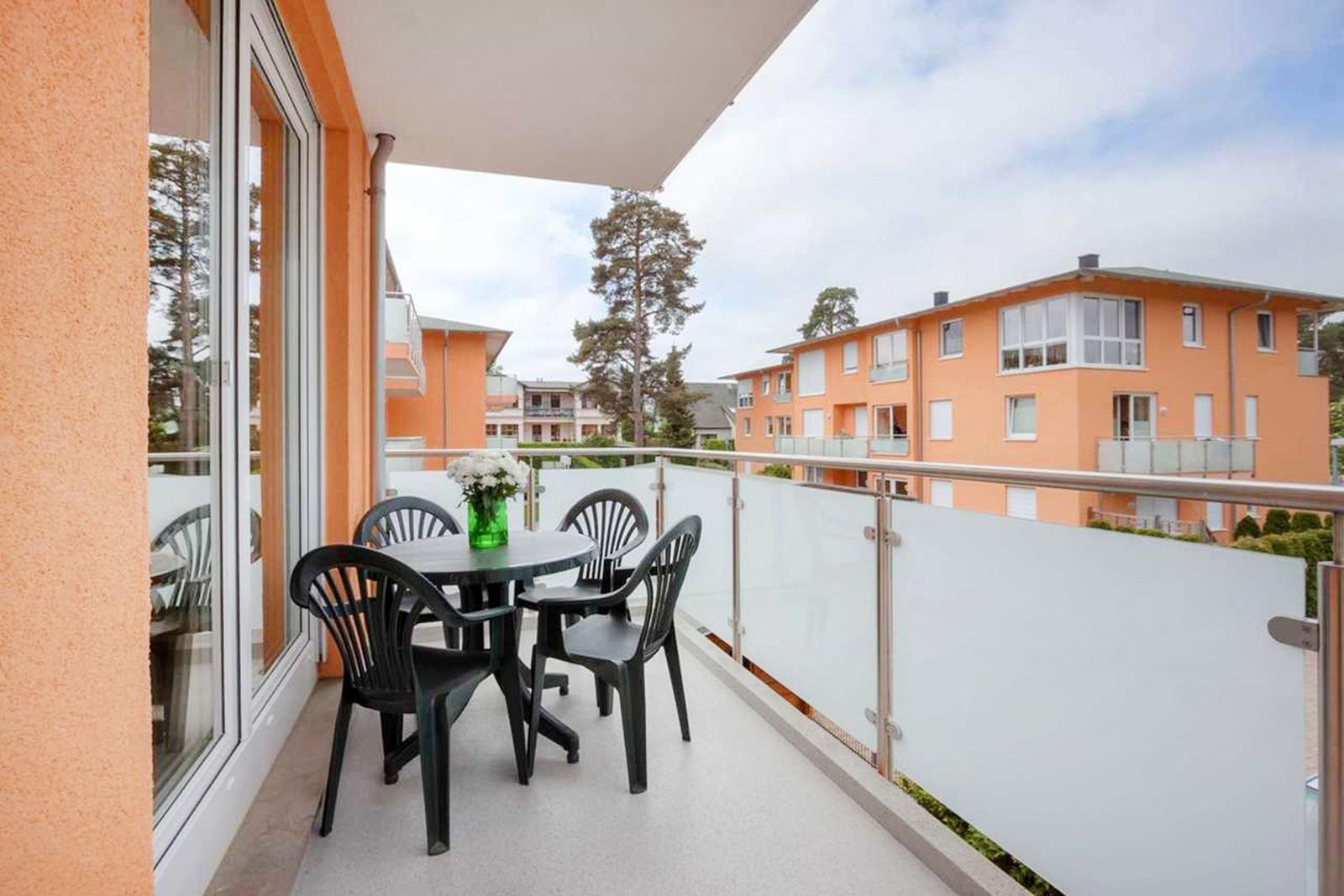 Terrasse mit Tisch und Stühlen, Glasgeländer und Blick auf orangefarbene Gebäude.