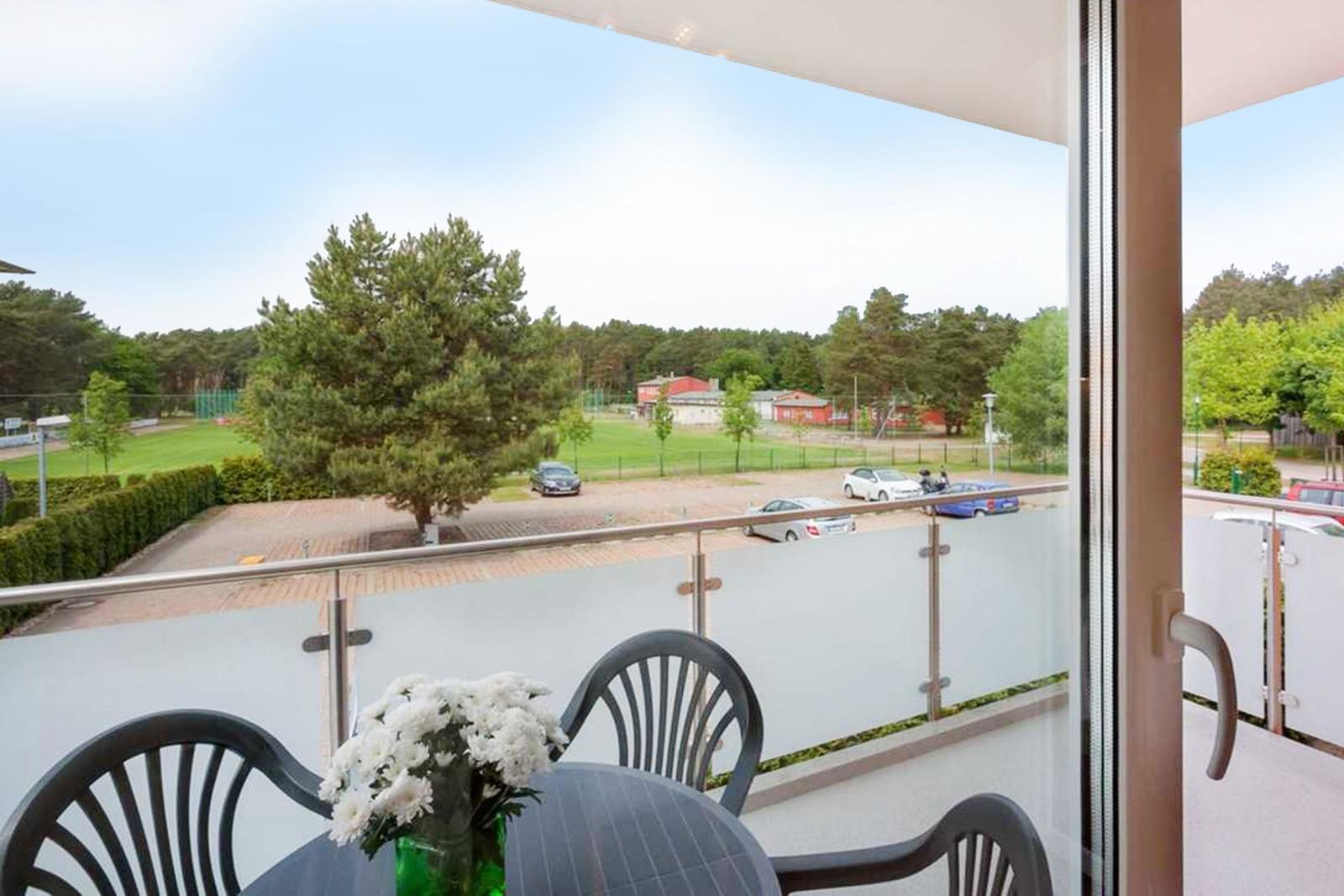 Balkon mit Tisch und Stühlen, Blick auf Parkplatz und Grünfläche.