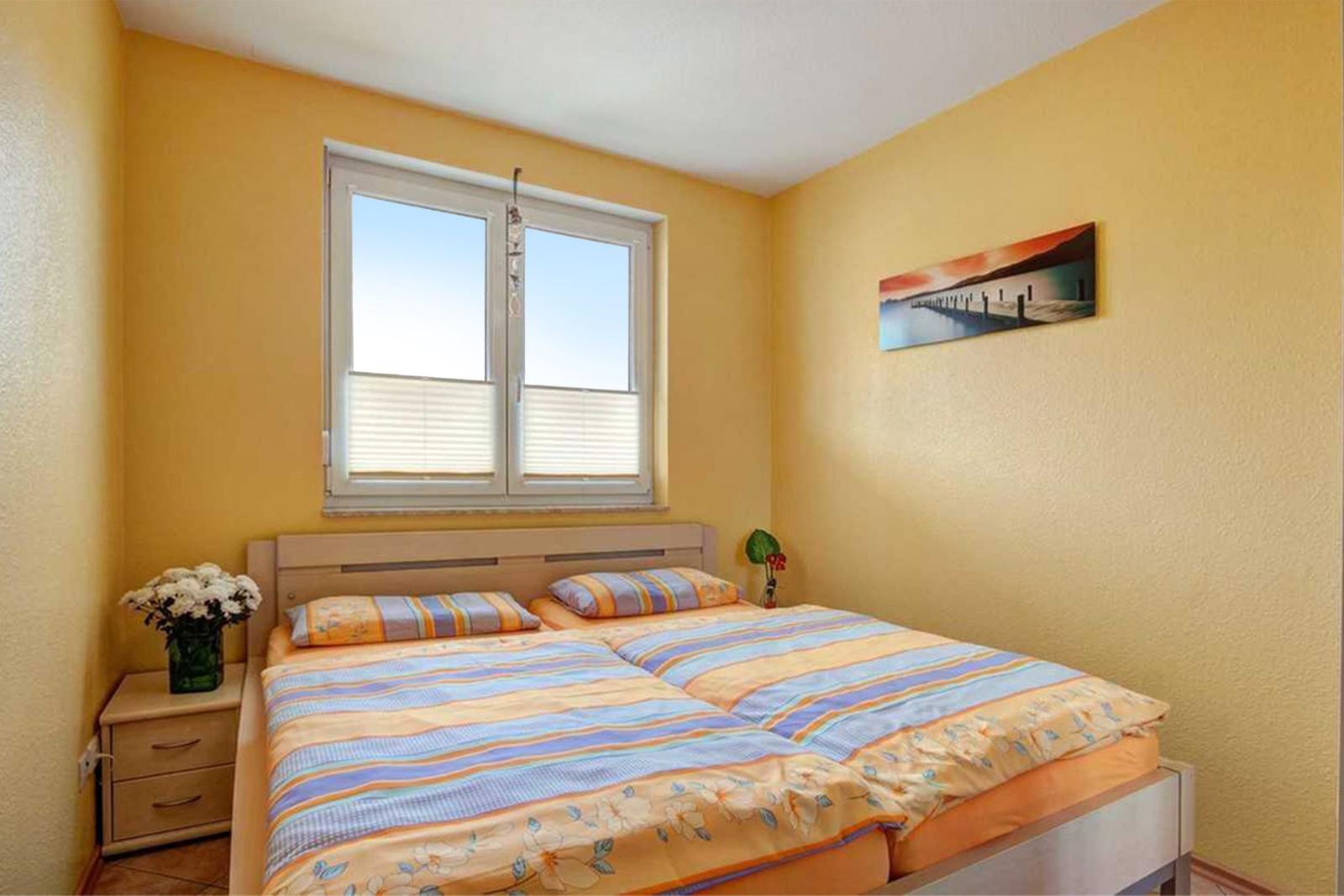 Schlafzimmer mit Doppelbett, Fenster und Wandbild.