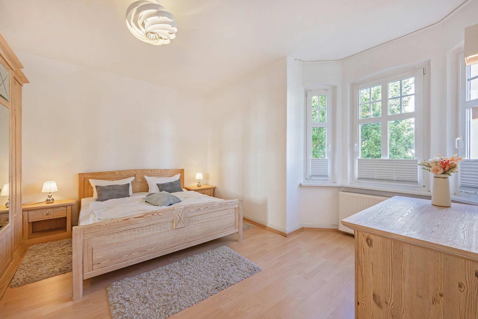 Bedroom with wooden bed, nightstands, and windows overlooking trees.