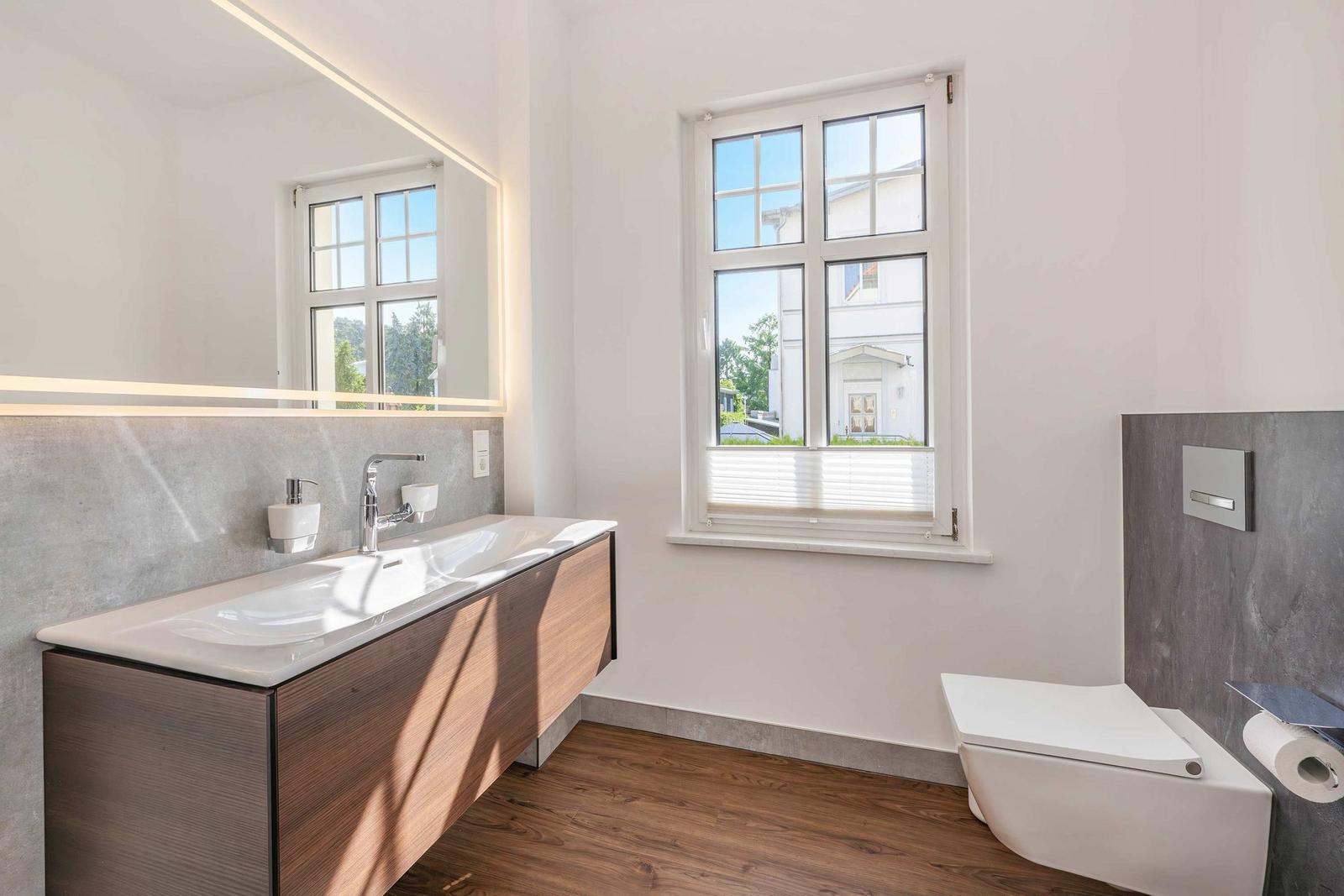 Bathroom with sink, mirror, and toilet. Wooden floor and window with view.