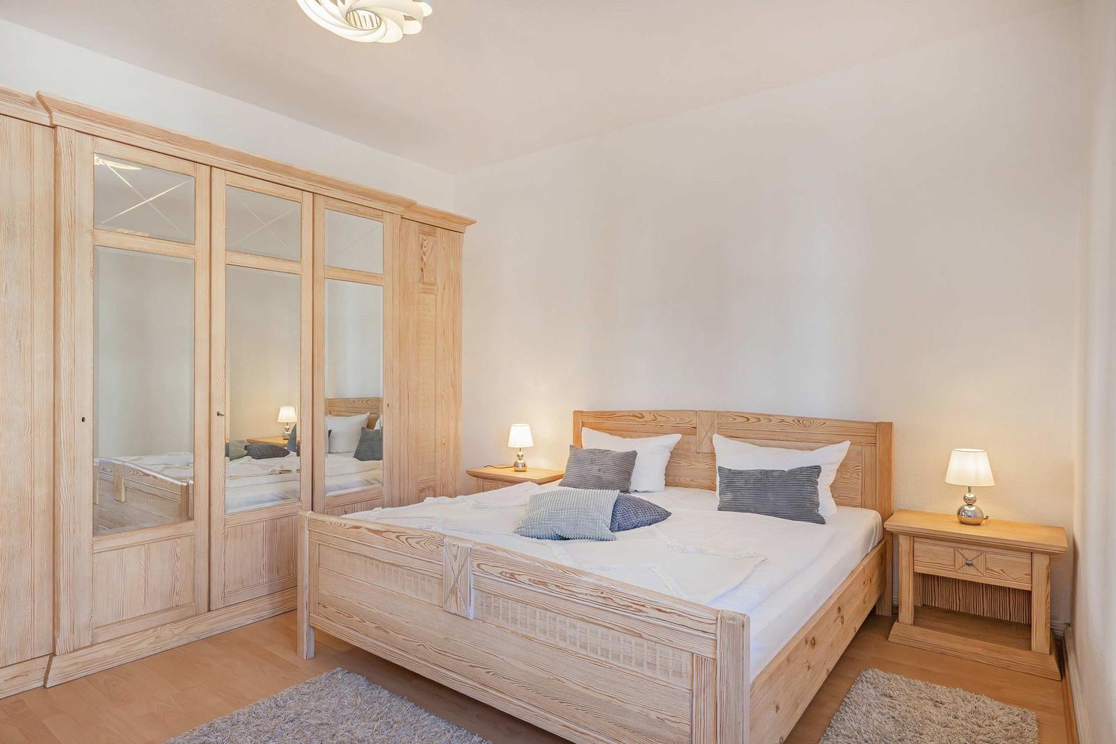 Bedroom with wooden bed, wardrobe with mirrored doors, and nightstands with lamps.