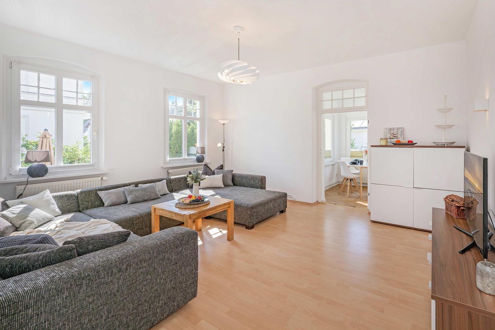 Living room with gray sofa, wooden table, and white walls. Passage to the kitchen.