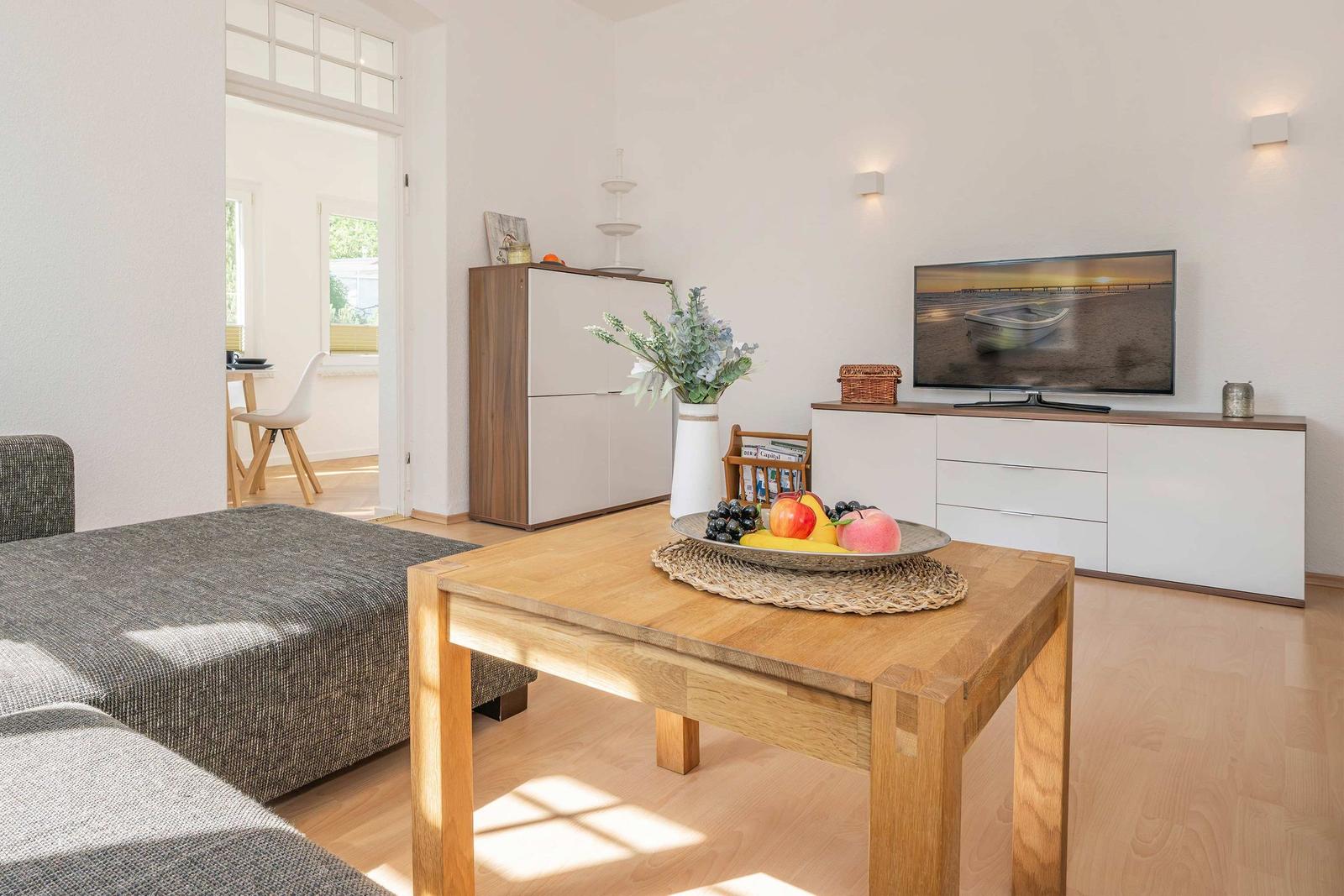 Living room with wooden table, sofa, and TV. Passage to kitchen and terrace.