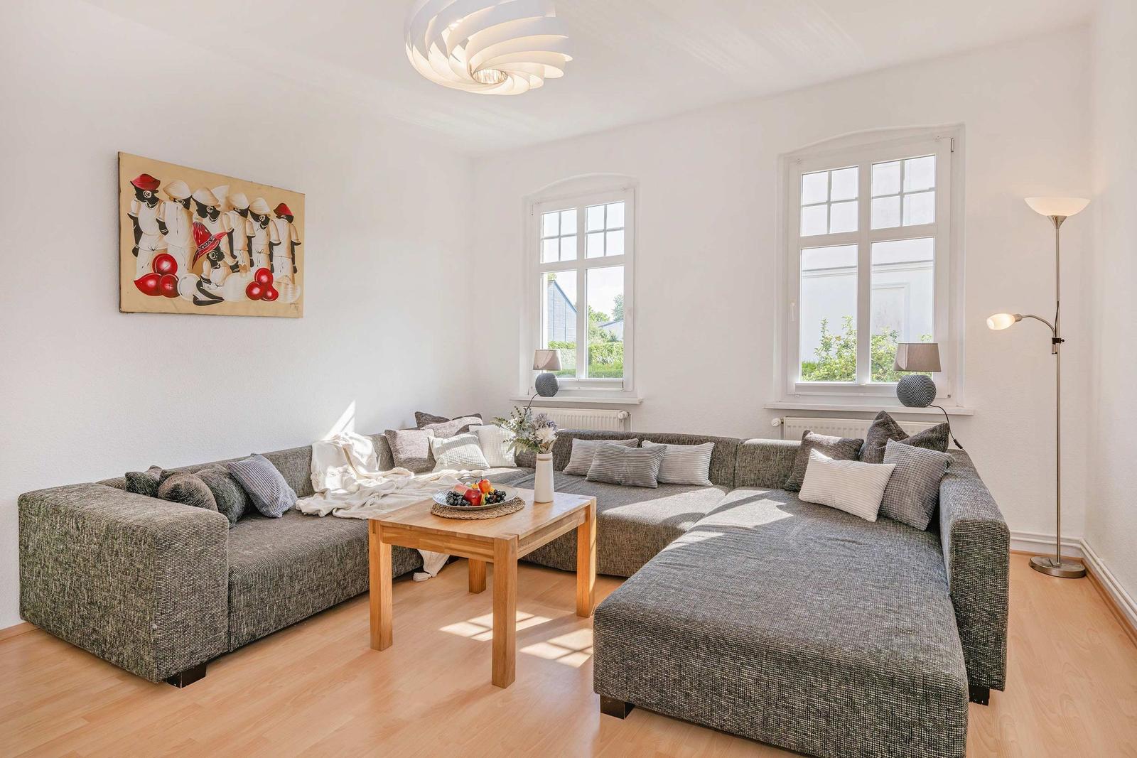 Living room with L-shaped sofa, wooden table, and two windows.