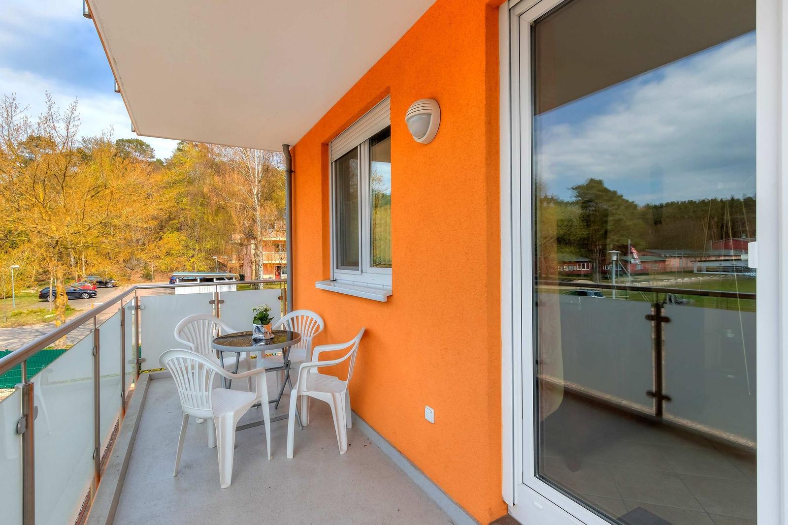 Terrasse mit weißem Tisch und Stühlen, orange Wand, Glasgeländer und Blick in die Landschaft.