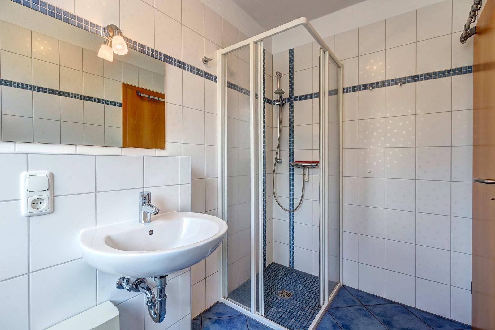 Badezimmer mit Dusche, Waschbecken und Spiegel an der Wand.