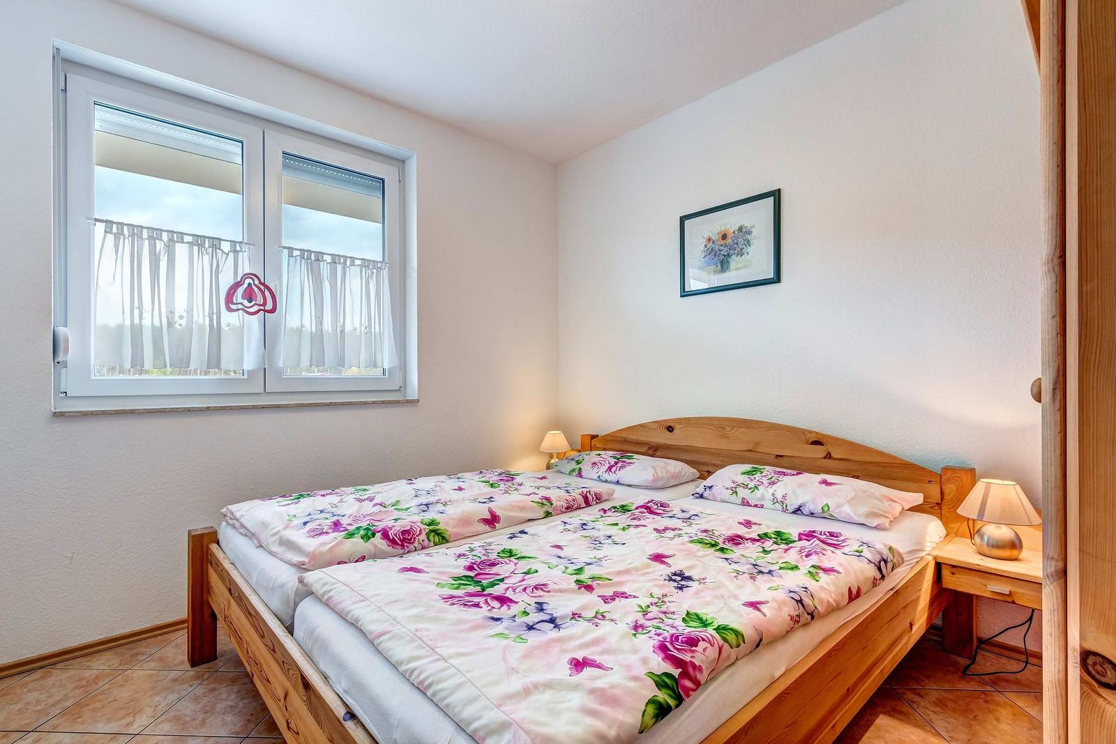 Schlafzimmer mit Holzbett, Fenster und Nachttisch.