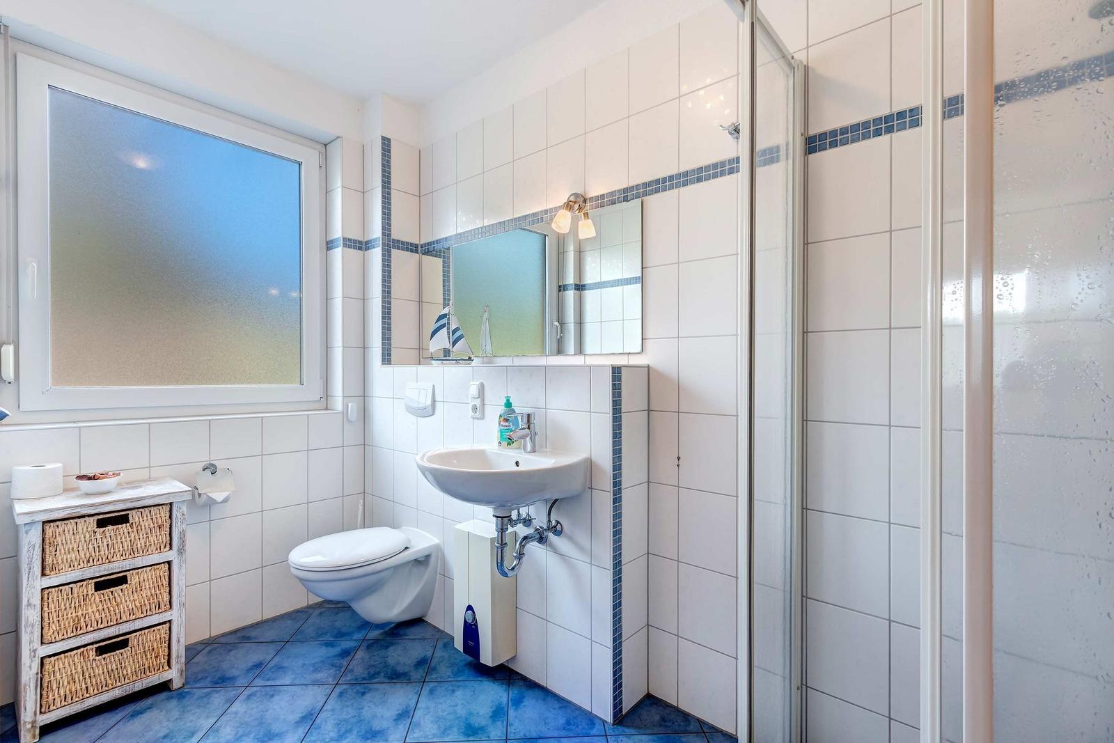 Badezimmer mit Dusche, Waschbecken und Toilette. Blaue Fliesen und Spiegel mit Segelboot.