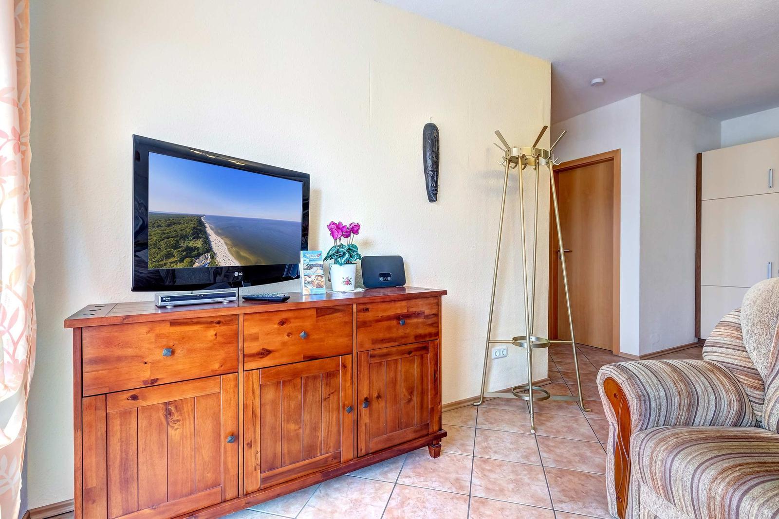 TV auf Holzschrank, Sessel und Kleiderständer im Wohnbereich.