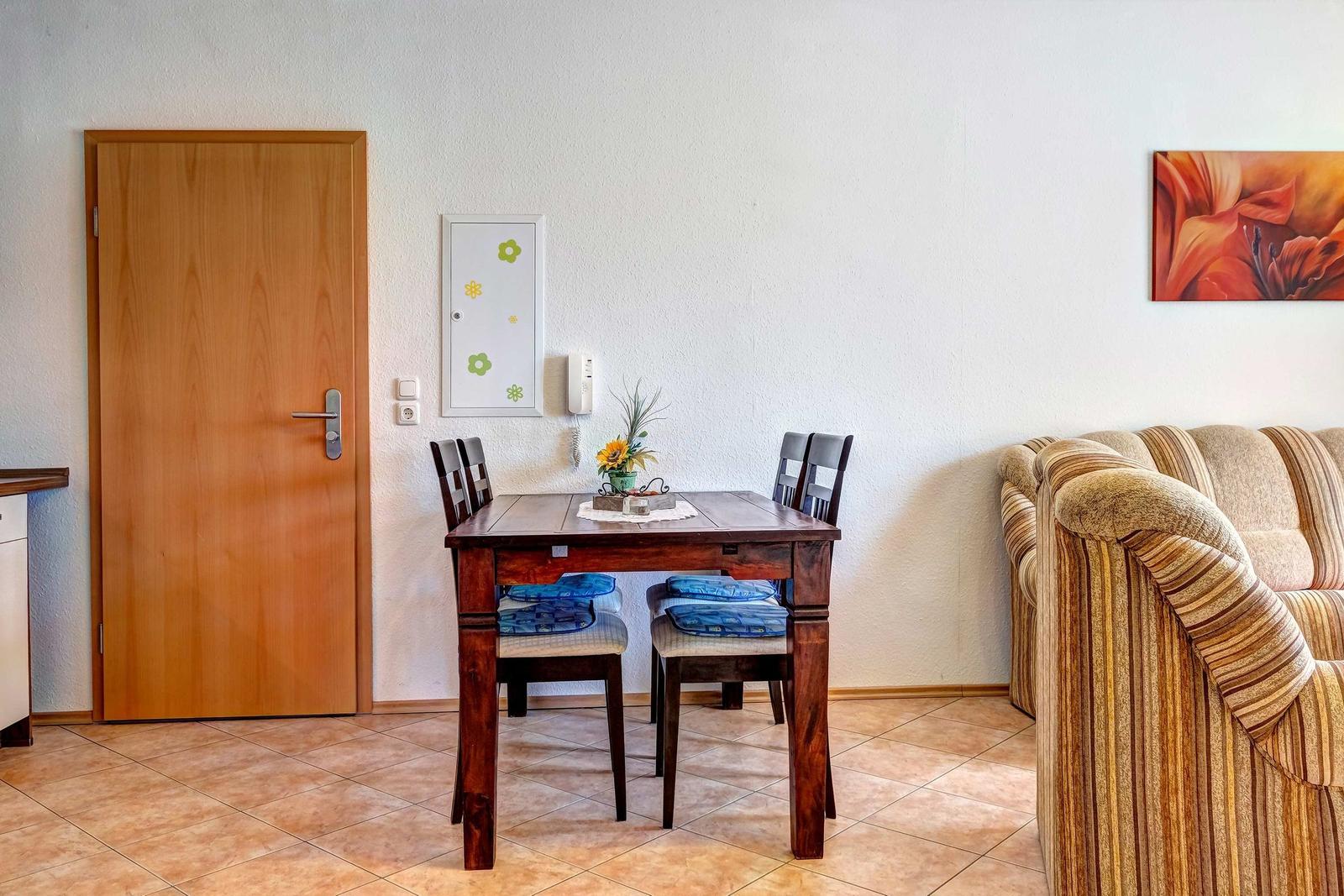 Essbereich mit Tisch, Stühlen und Sofa. Tür, Wand und Boden sind sichtbar.