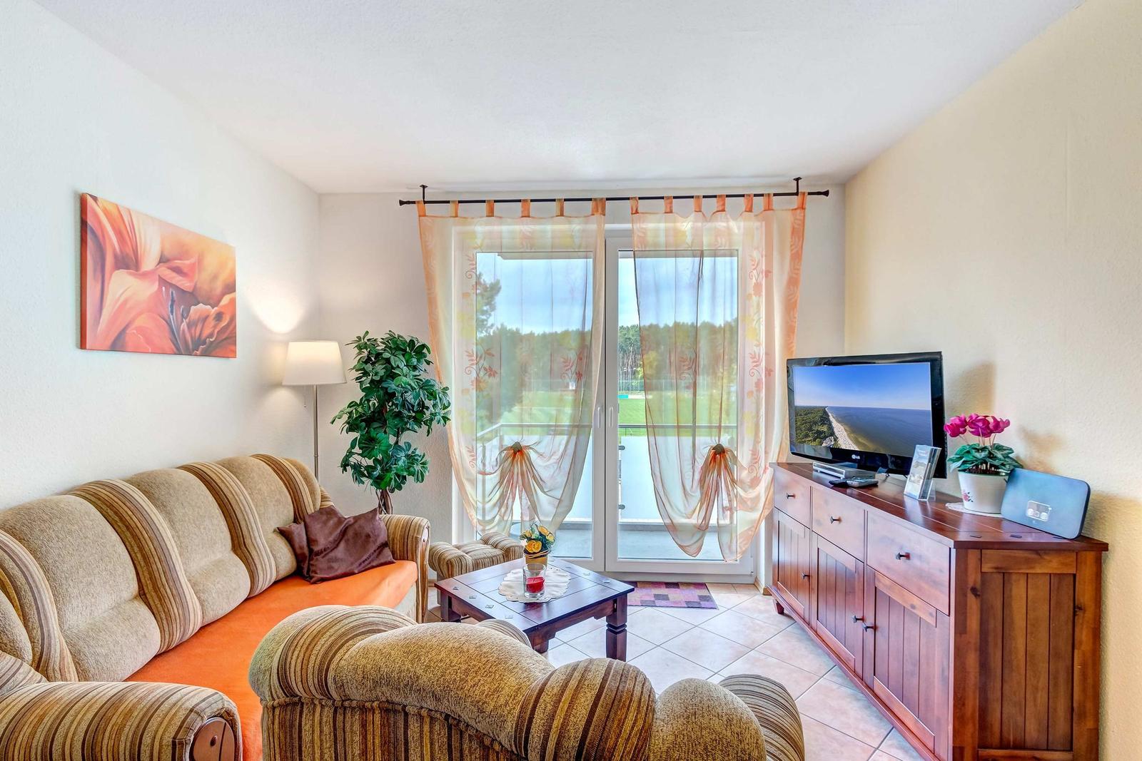 Wohnzimmer mit Sofa, Fernseher und Balkontür mit Blick auf Grünfläche.