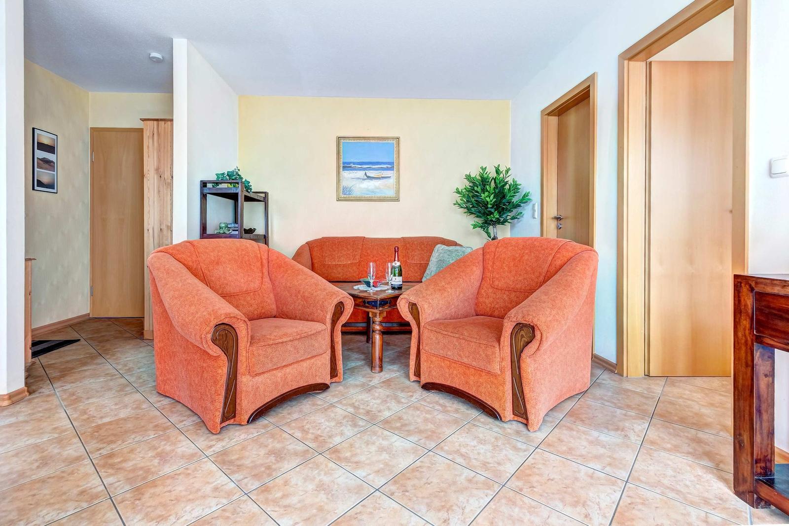 Wohnzimmer mit zwei orangefarbenen Sesseln, einem Sofa und einem Tisch.