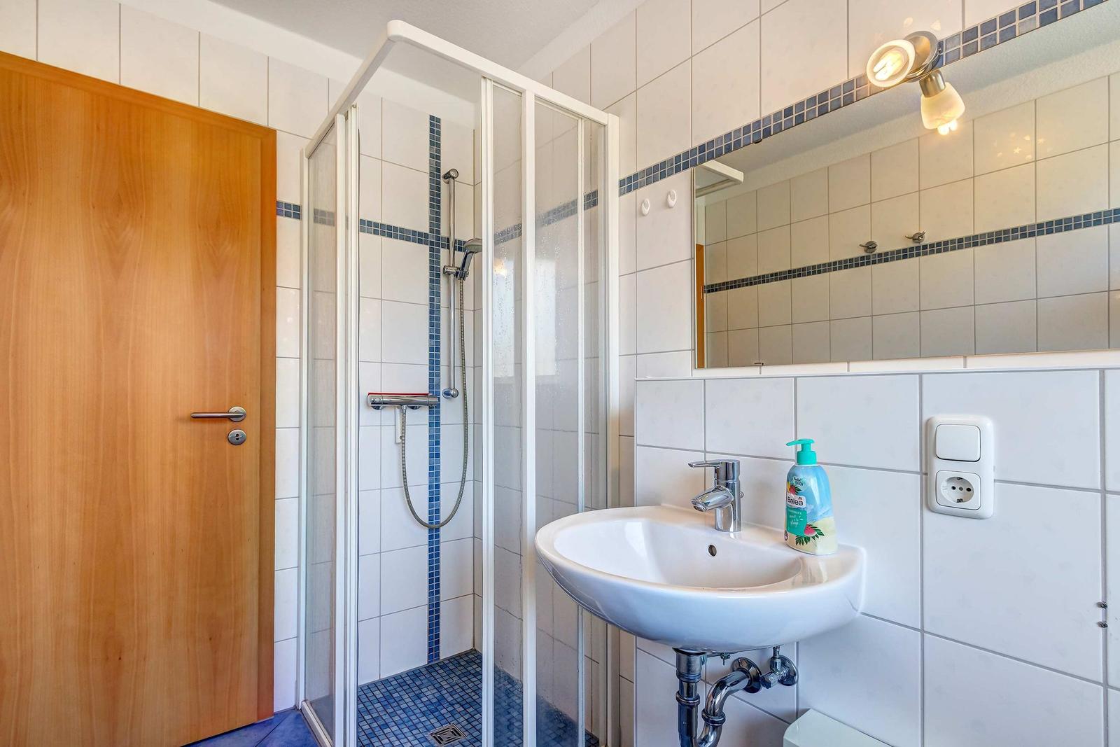 Badezimmer mit Dusche, Waschbecken und Spiegel