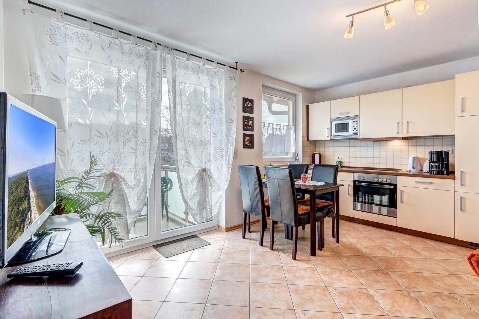 Wohnküche mit Essbereich, Balkon und TV. Küchenschränke, Herd und Mikrowelle sichtbar.